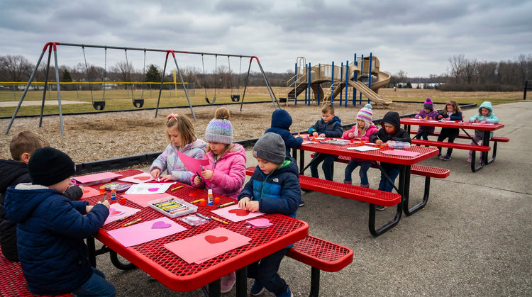 Kids making valentines cards by their school playground at red picnic tables
