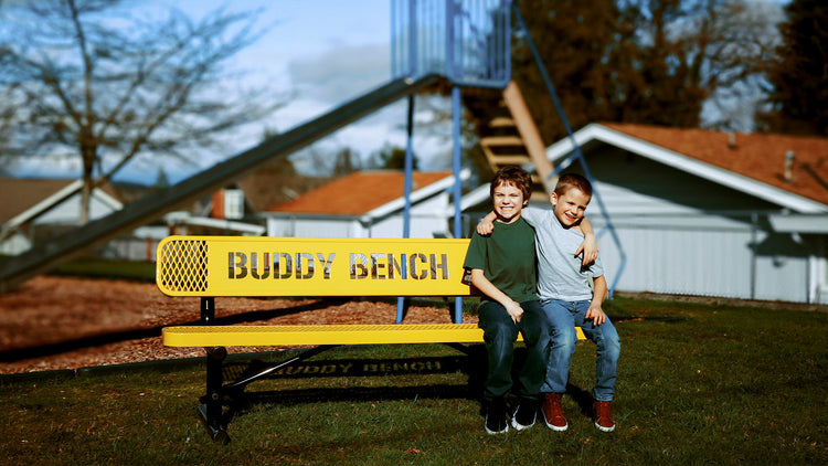Two children sitting at a Buddy Bench at a school playground having fun