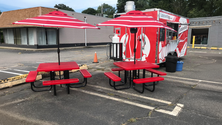 two red picnic tables at a food truck in a parking lot