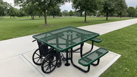 A green ADA accessible picnic table in a park with a wheelchair at the ADA end of the table
