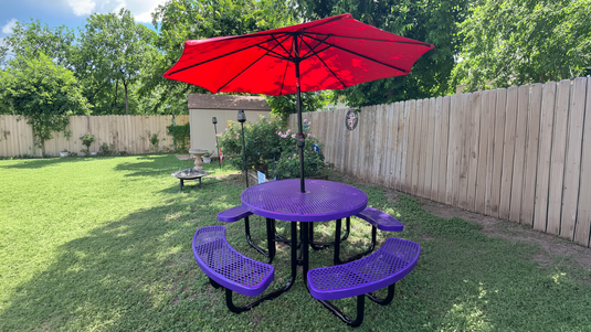 A purple picnic table with a red umbrella in a backyard on a sunny day