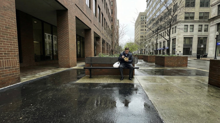 A man having lunch on a bench outside a business plaza