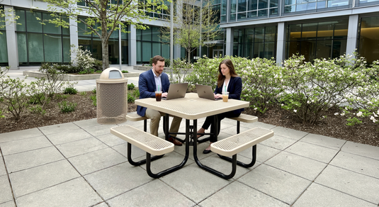 two workers sitting at a table outside with their laptops