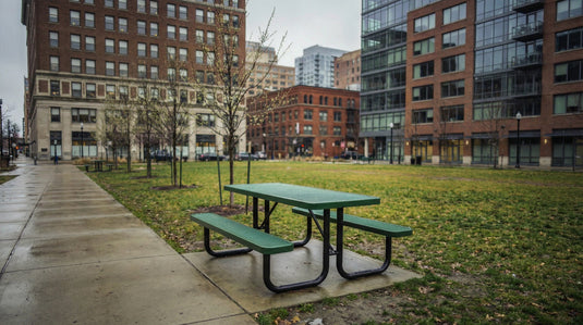 A green picnic table in a city park with tall buildings in the background
