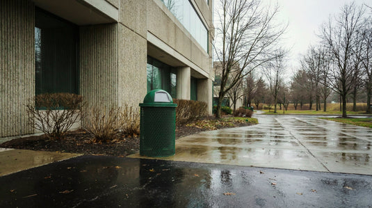 A green trash can in a municipal campus on a rainy day
