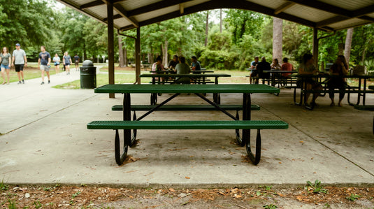 Green metal picnic table under a park pavilion with people in the background.