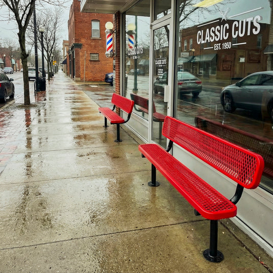 Two red benches outside of a barber shop in the rain